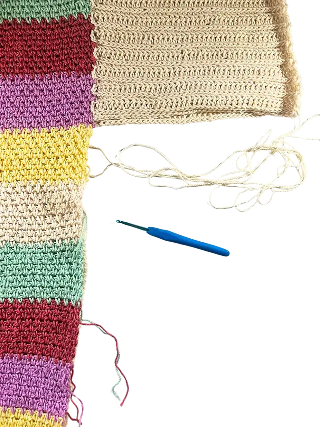 Colourful front and back crochet sweater panels laid side by side with a yarn needle and yarn tail positioned at the edge, ready to begin seaming along the side.