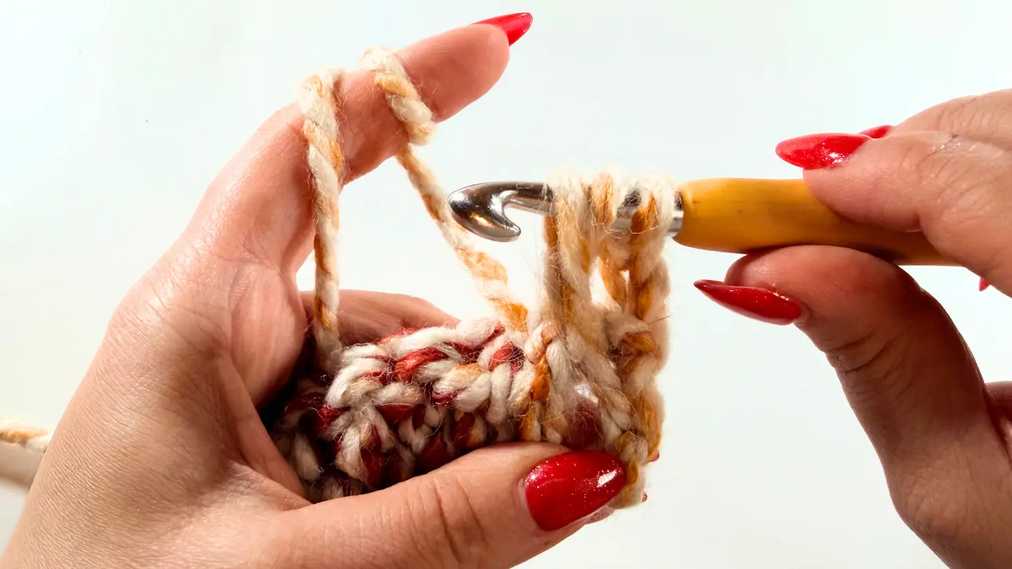 Demonstration of pulling yarn through loops on crochet hook while forming stitch for beginner-friendly chunky hat pattern.