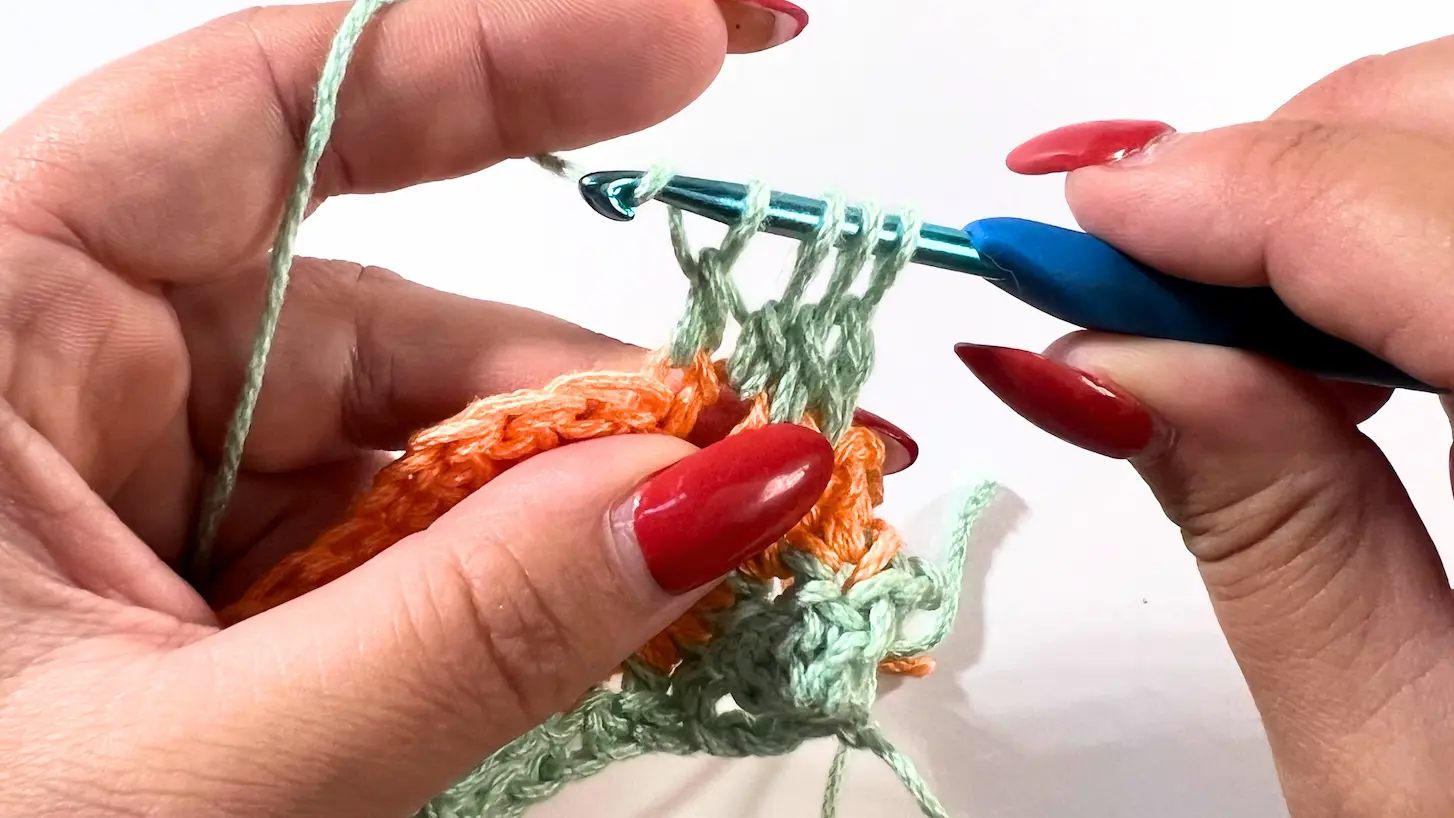 Crocheter holding the hook with four loops on it, ready to yarn over and pull through all loops to complete the 4DC cluster at the start of row 4.