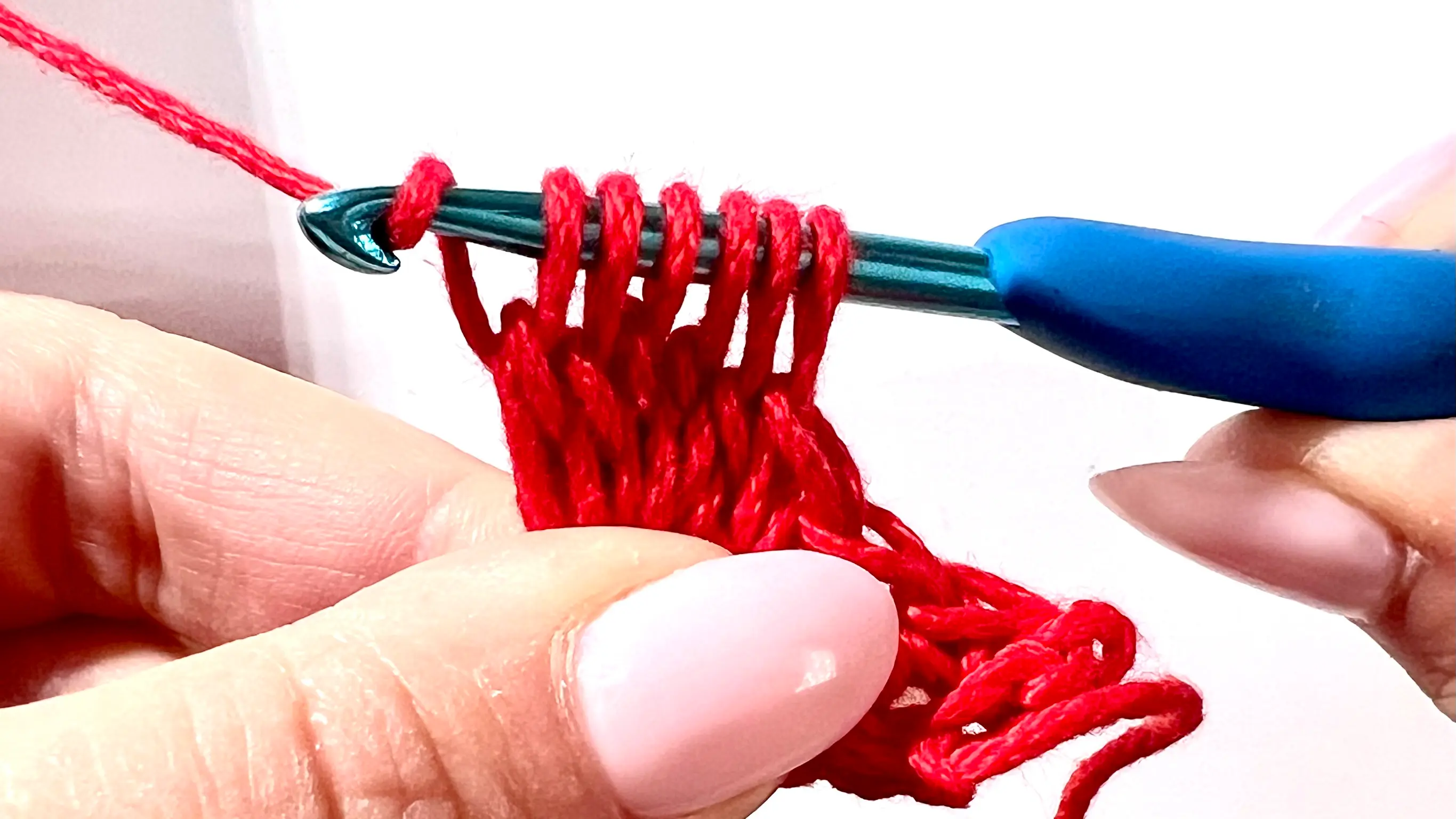 Crocheter forming a bobble stitch in red yarn, with several incomplete double crochets on hook before closing the cluster.