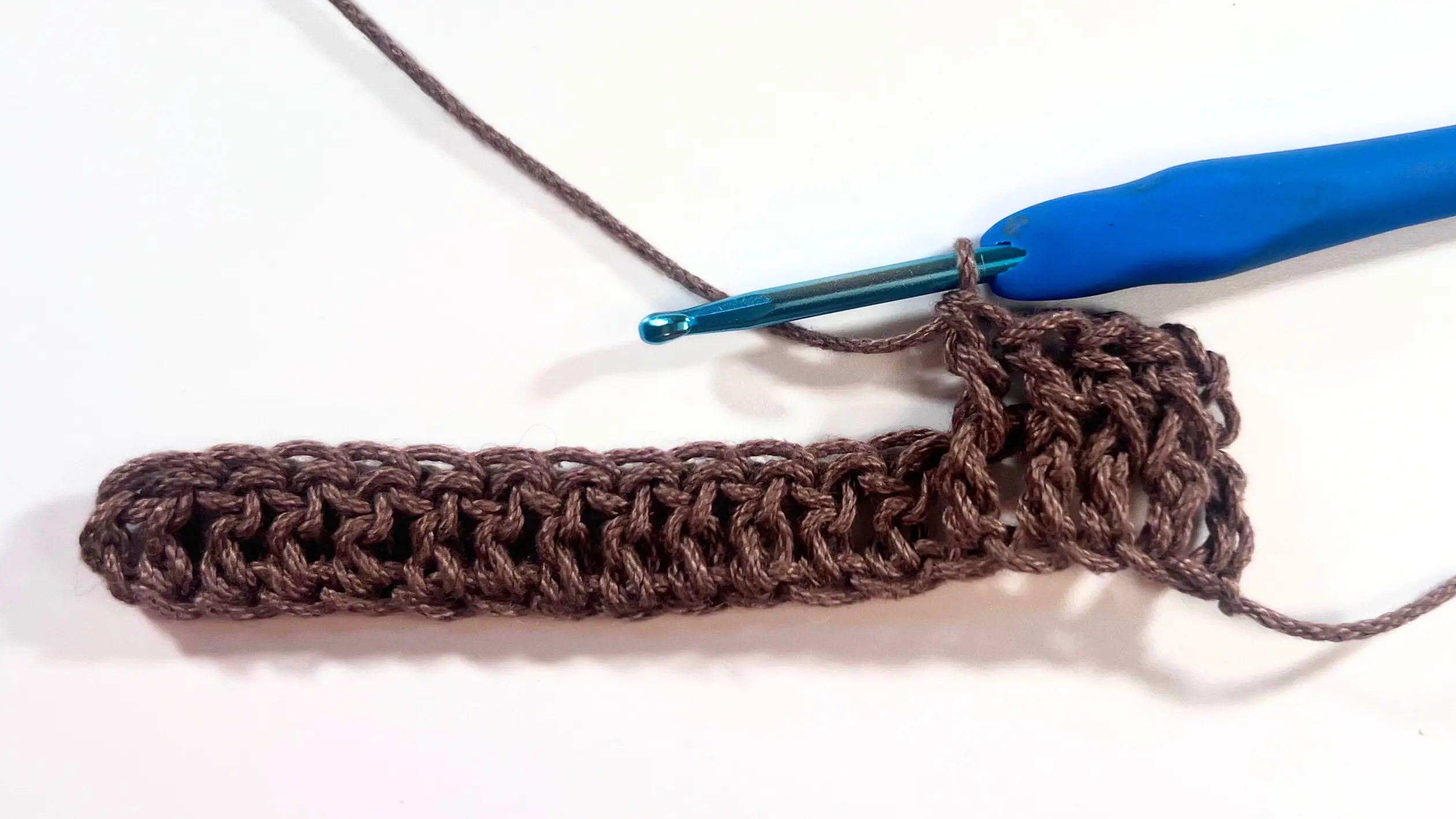 Partially completed row with four Front Post Double Crochets visible, showing the start of the basket weave texture in brown yarn.