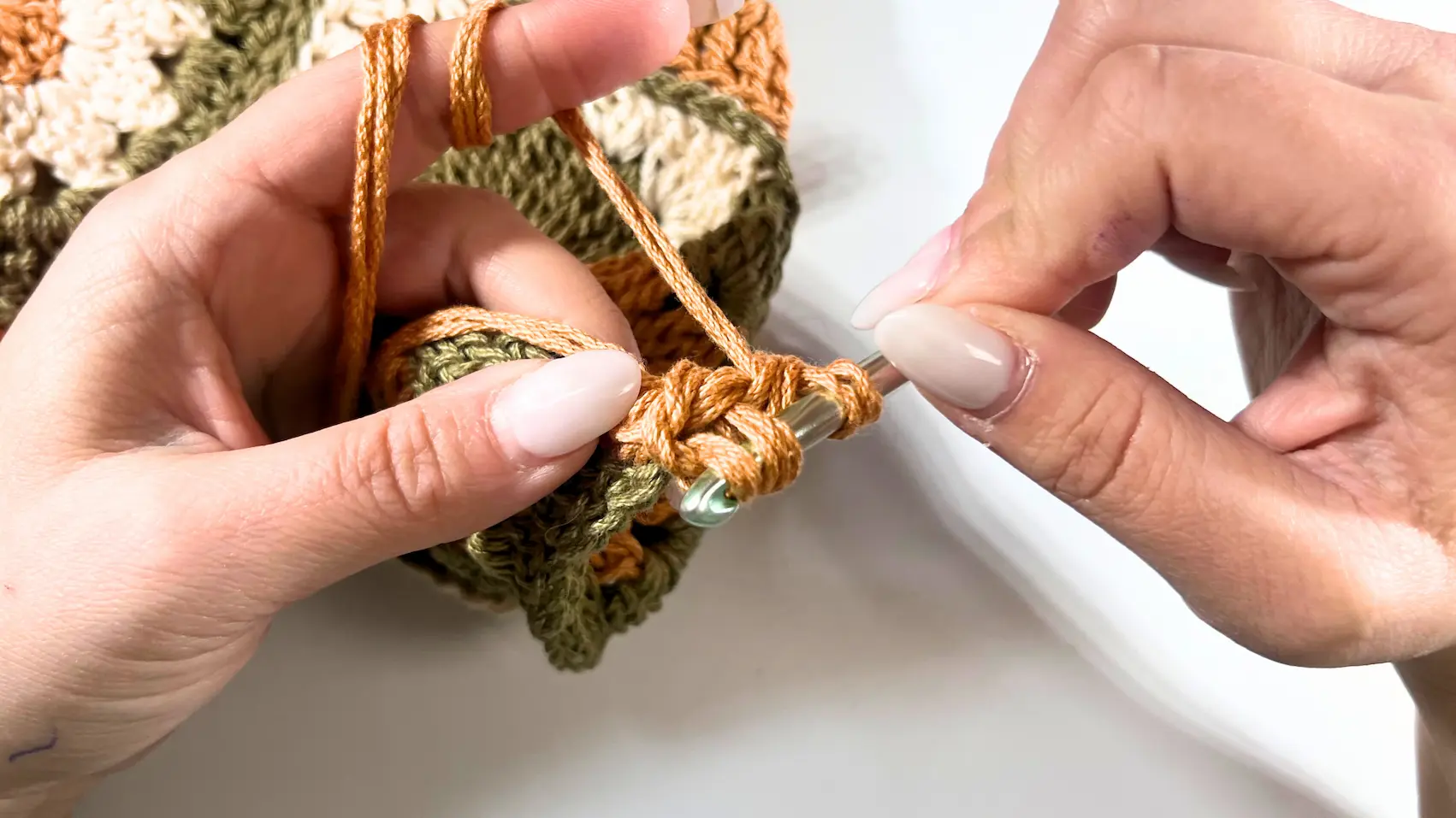 The crocheter pulls yarn through the stitches as they continue building the orange strap.