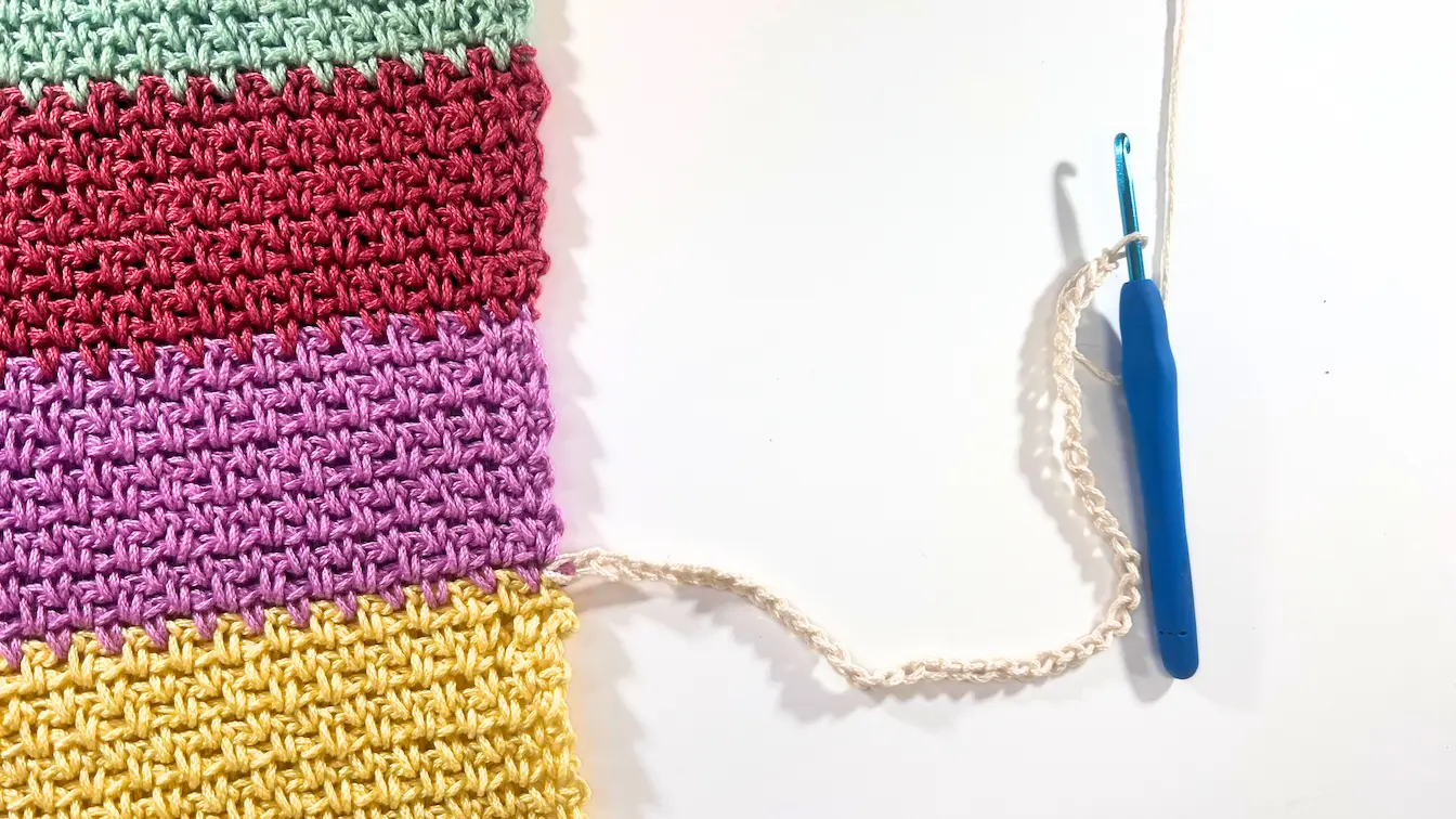 Colourful crochet sweater panel with a new cream foundation chain attached to the side, ready to start the sleeve worked in rows from the side seam.