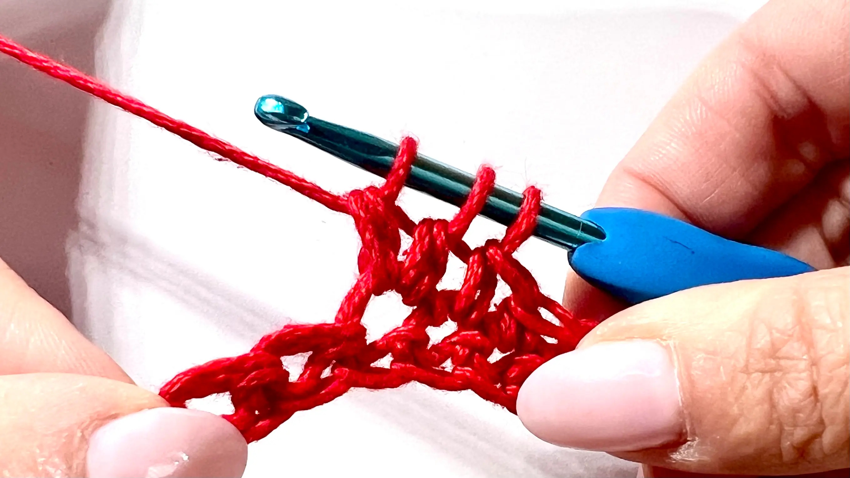 Crocheter forming a bobble stitch in red yarn, with several incomplete double crochets on hook before closing the cluster.
