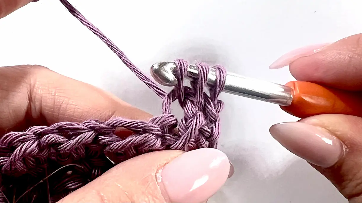 A half-finished stitch in the decrease row of a C2C Even Moss project, showing four loops on the hook. The yarn is tensioned and ready for a yarn over to complete the stitch.