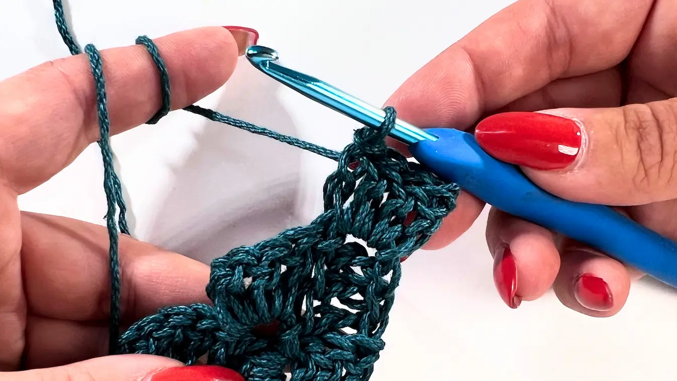Crochet C2C tutorial – crochet hook and teal yarn positioned after slip stitches, ready to continue with the first square of the row.