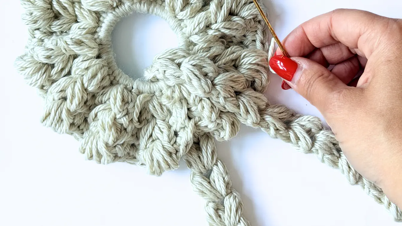Position the finished crochet heart tail between two puff stitches on the crochet heart scrunchie.
