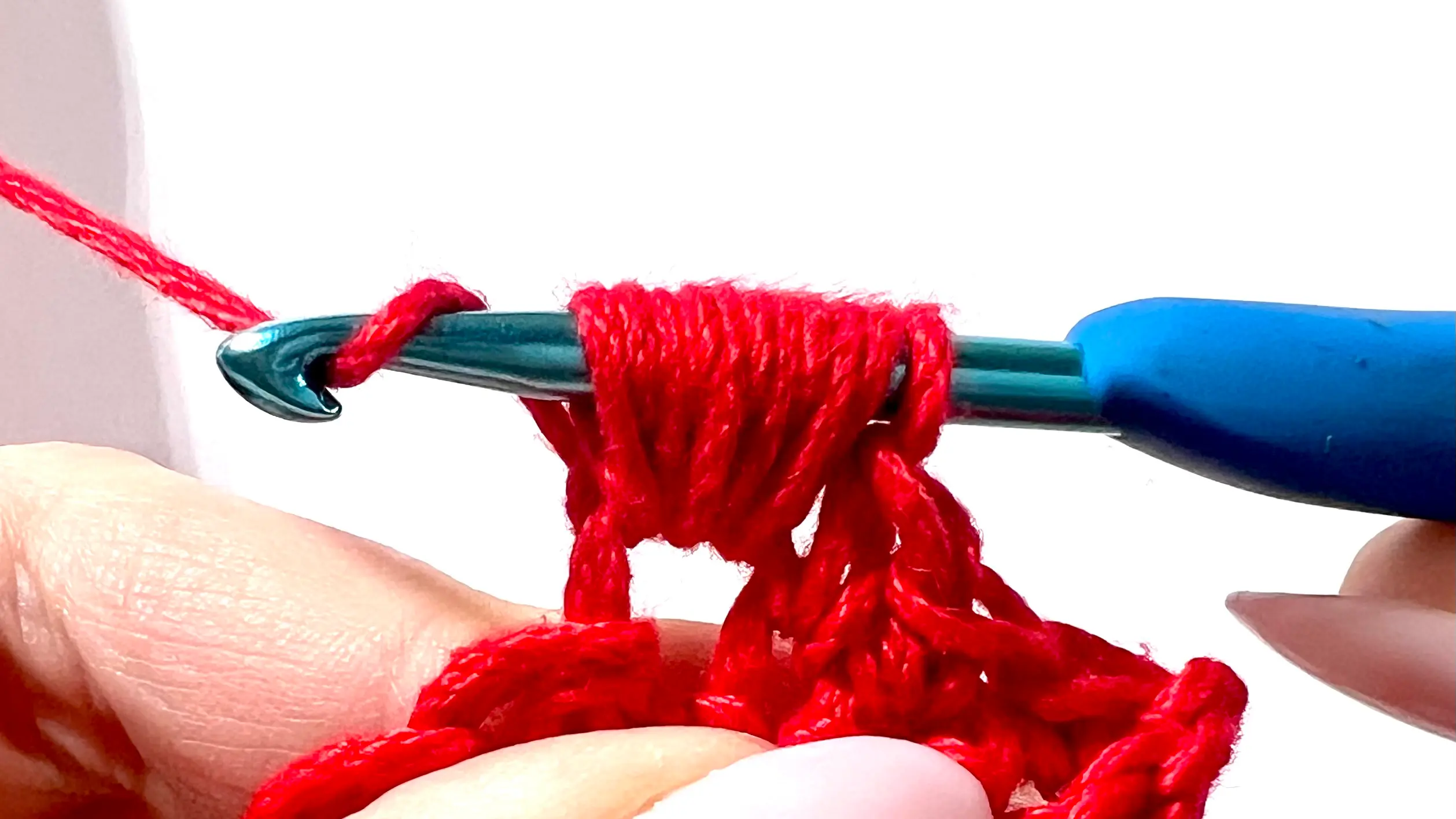 Crocheter creating a puff stitch with red yarn, showing yarn overs and multiple loops on hook before pulling through.