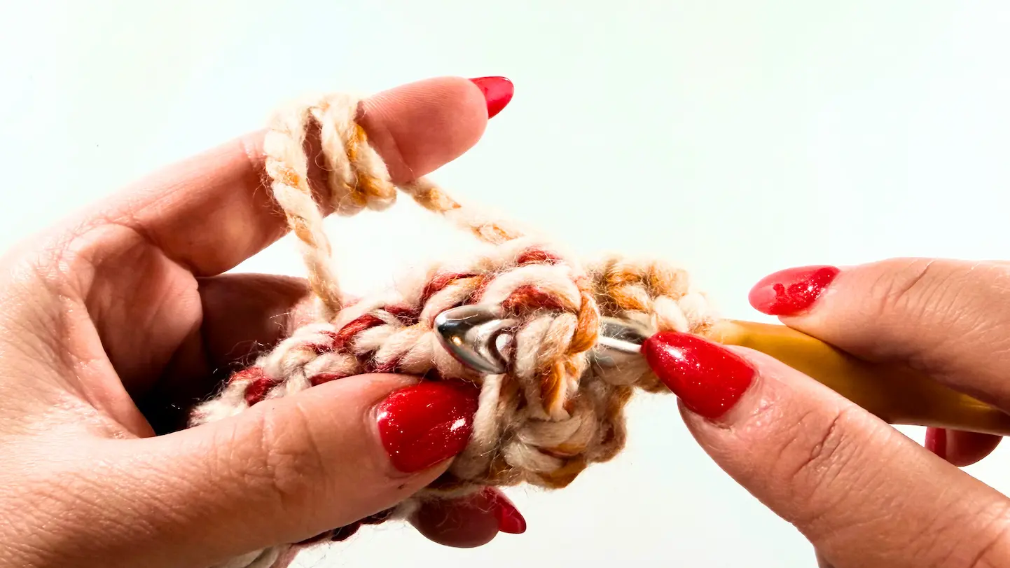 Close-up step of inserting crochet hook into stitch while working second row of chunky crochet beanie with super bulky yarn.