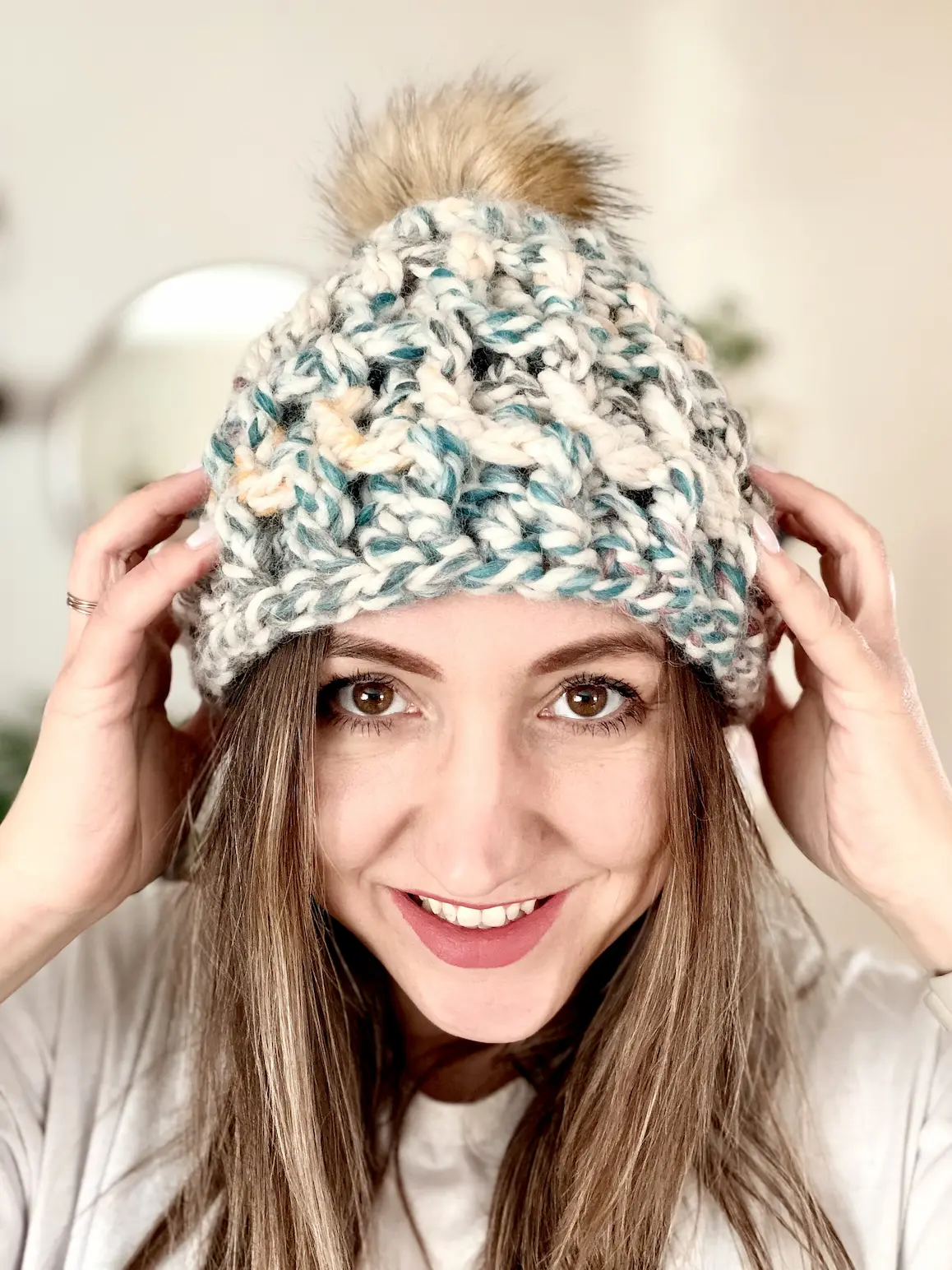 Woman modeling textured chunky crochet beanie in super bulky yarn with faux fur pompom and ribbed detail.