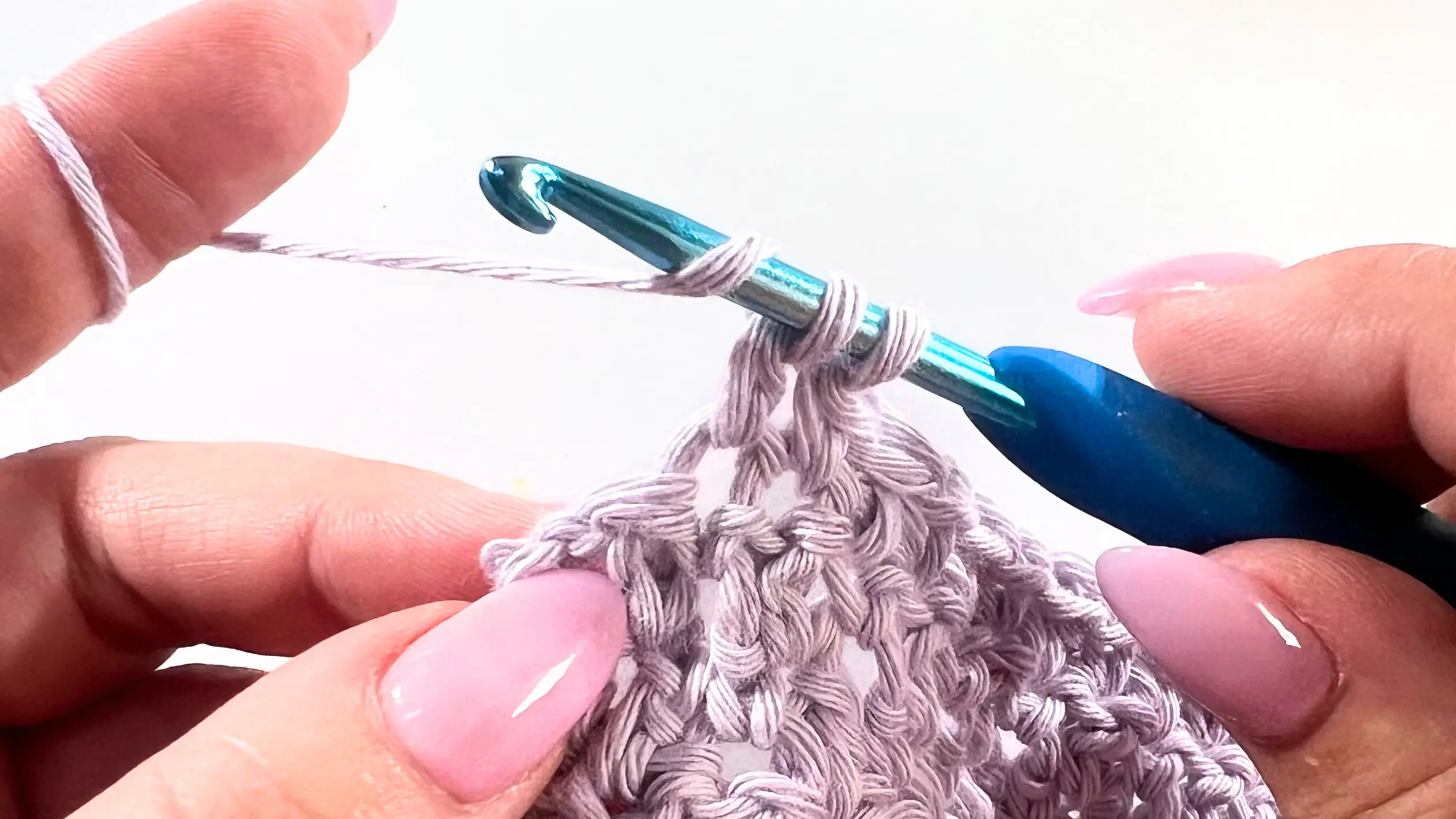 Crochet hook with yarn over, pulling through the first two loops while working a DC2tog decrease in the Lemon Peel Stitch C2C baby washcloth.
