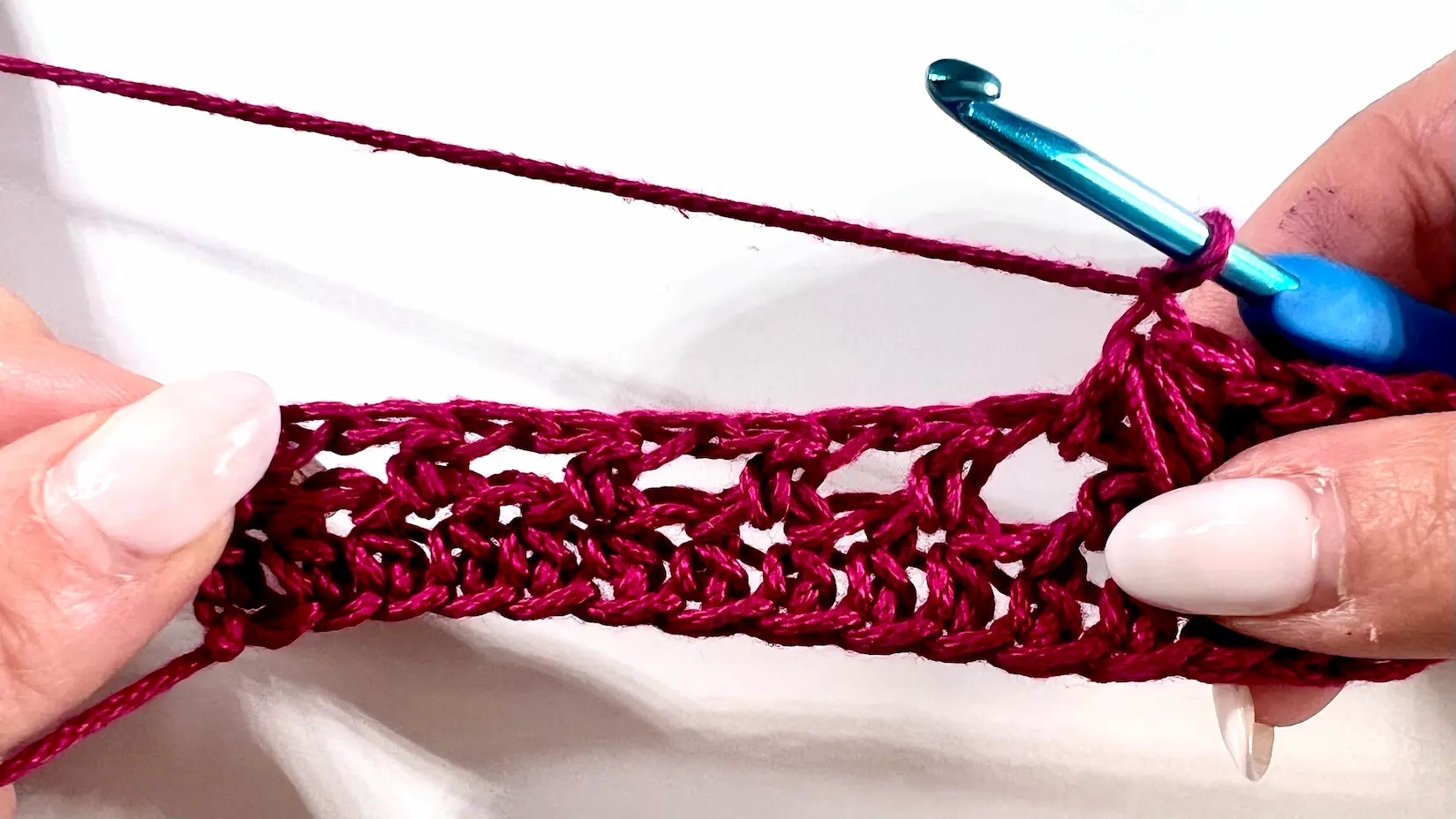 Close-up showing how to crochet the feather stitch step-by-step using fuchsia yarn and a blue crochet hook — part of a textured stitch tutorial.