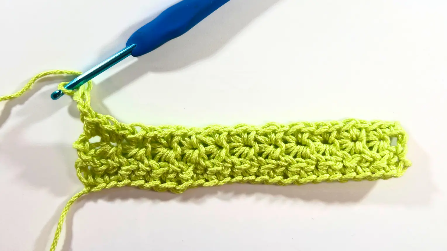 Completed Row 3 shown from above with bright green yarn and blue hook, clearly displaying the structure of the stitches.