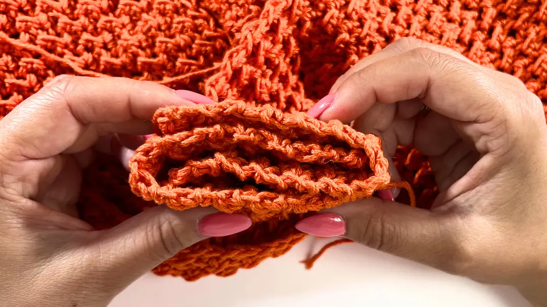 Hands holding folded edges of the crochet fabric, aligning stitches for sewing the twist in the summer top.