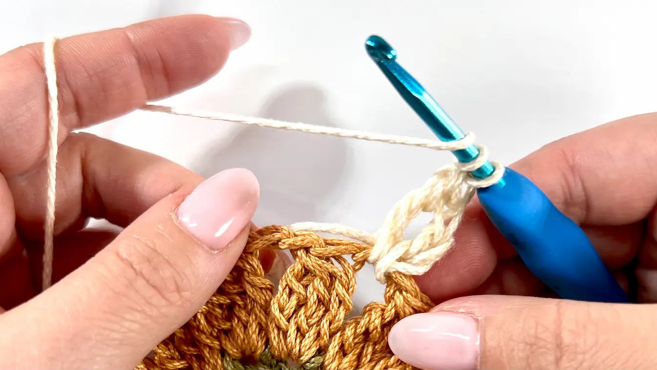 Crocheting the first double crochet group with cream yarn into a chain space of the Daisy Square.
