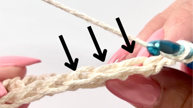  Close-up of a crochet foundation chain with arrows pointing to the back loops, showing where the hook should be inserted for HDC in back loop only.
