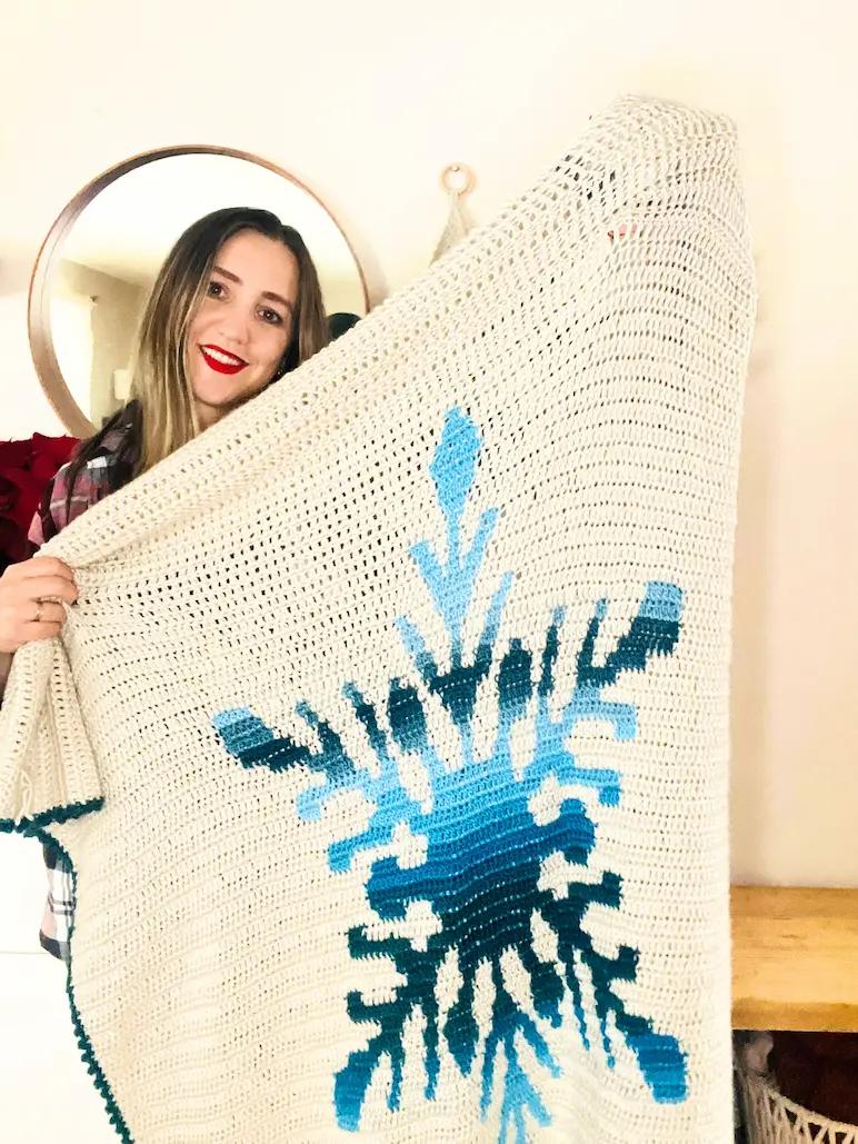 Lenka from Happy Heartsy holding the Northern Flakes crochet blanket with a large blue snowflake design.