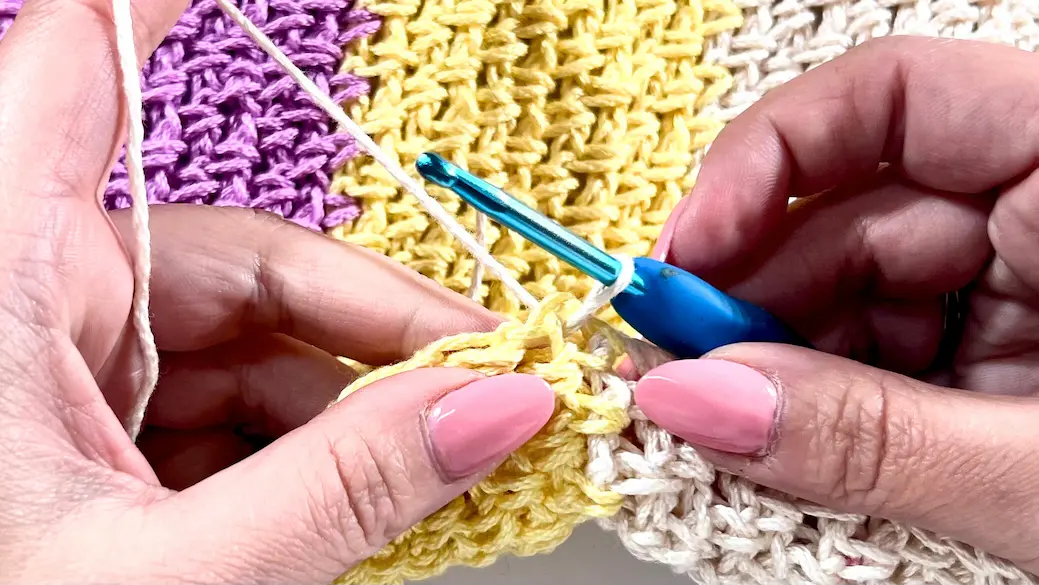 Crochet hook inserted into the first stitch with the new yarn colour already joined, ready to begin working across the row with the new yarn.