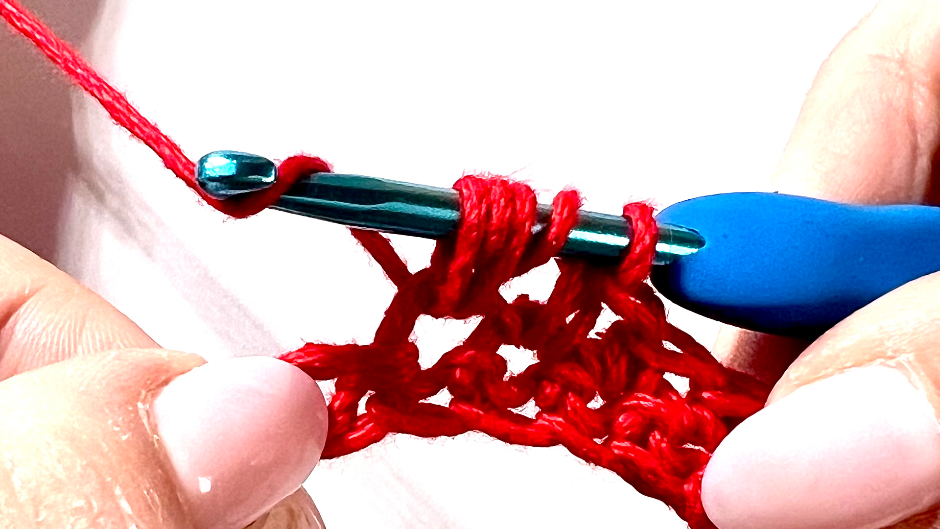 Crocheter creating a puff stitch with red yarn, showing yarn overs and multiple loops on hook before pulling through.
