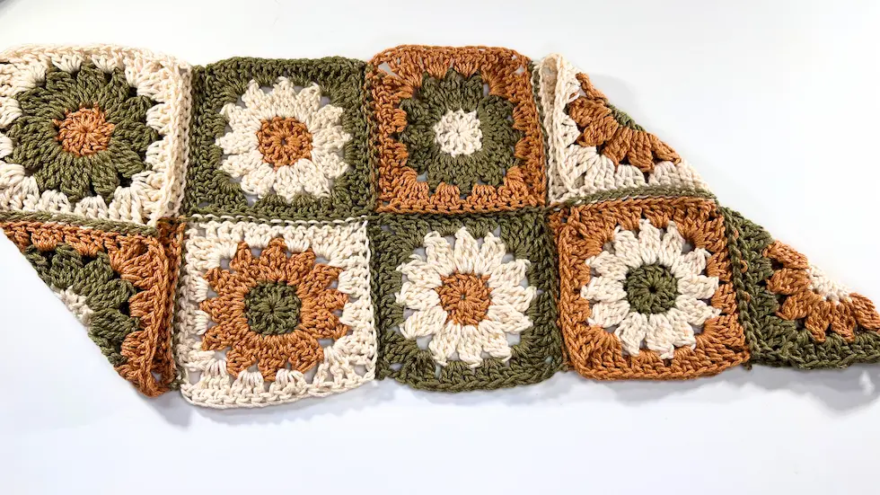 Both outer corners of the crochet square section are folded in, creating a V-shape with overlapping triangles.