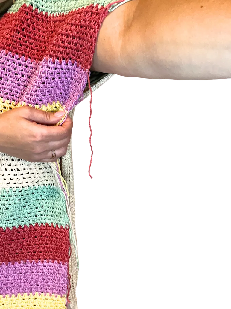 Close-up of a crochet panel held against the upper arm, demonstrating how to measure and fit the sleeve width by marking the desired armhole depth.