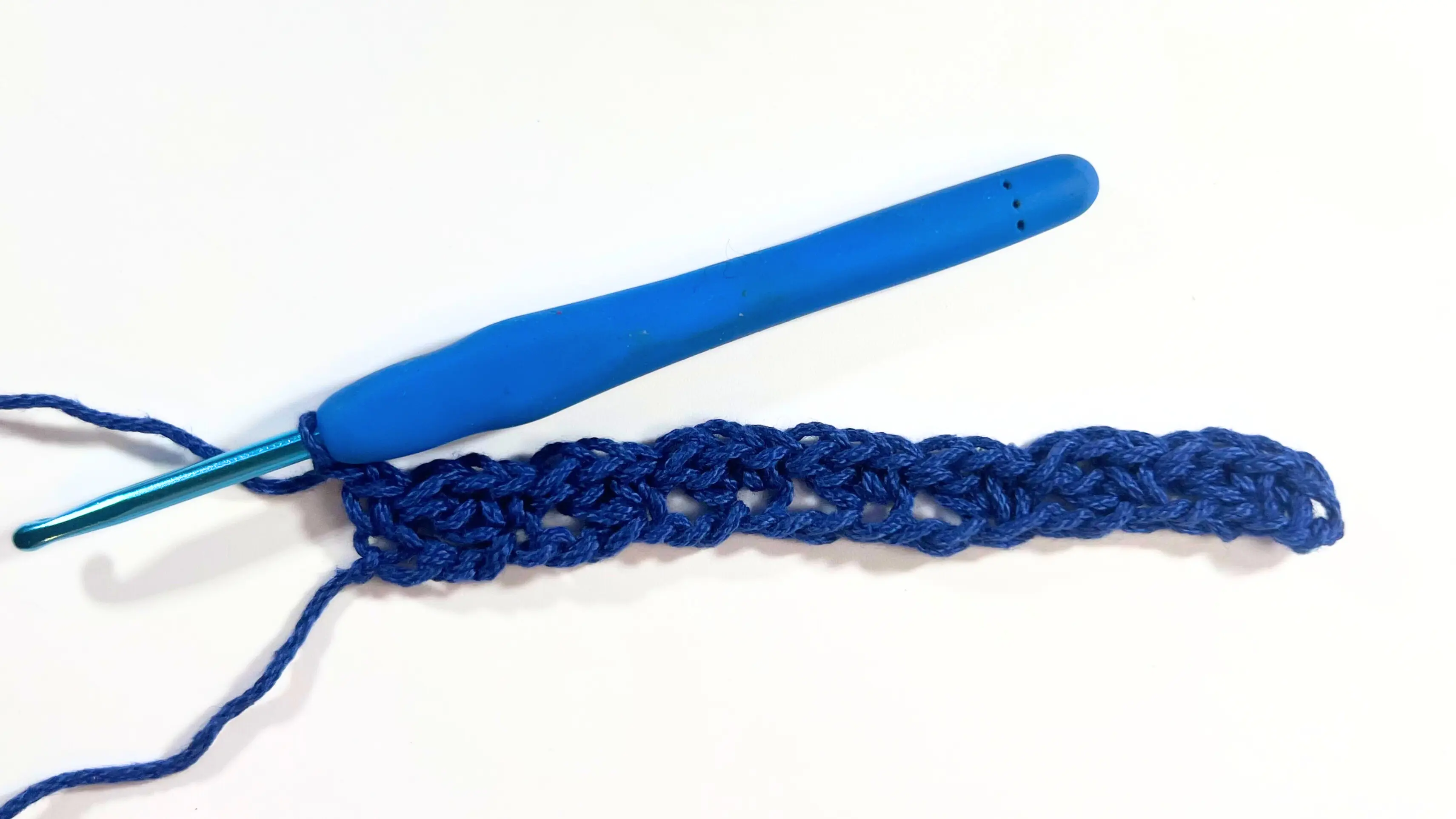A completed first row of wattle stitch in blue yarn, with the hook resting in the final stitch on the right.