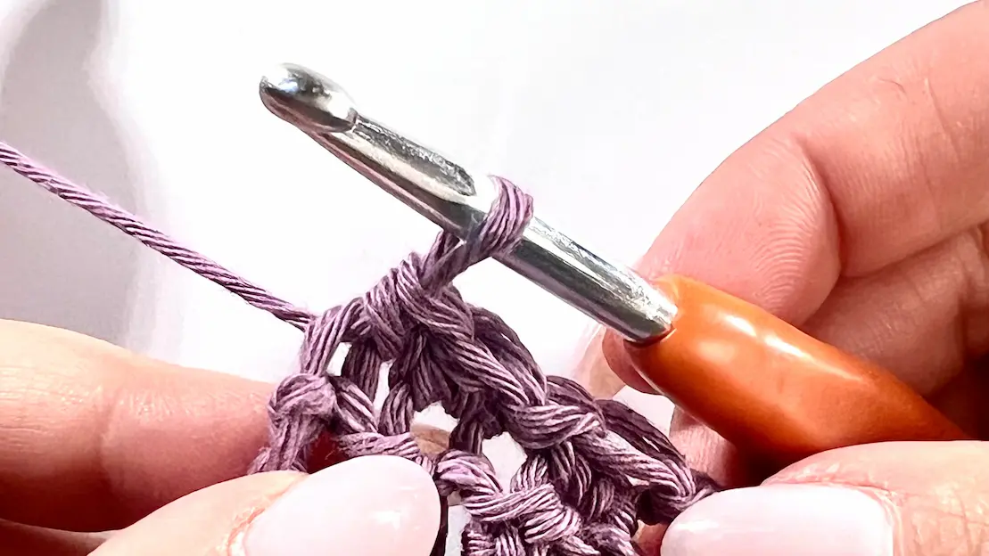 The last stitch of a diagonal row is complete in a C2C Even Moss Stitch project. The crochet hook with orange handle is resting in the active loop, ready for the next row.