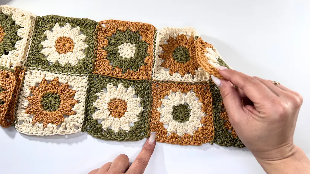 Hands folding the opposite side of the crochet square section inward, mirroring the first triangle fold.