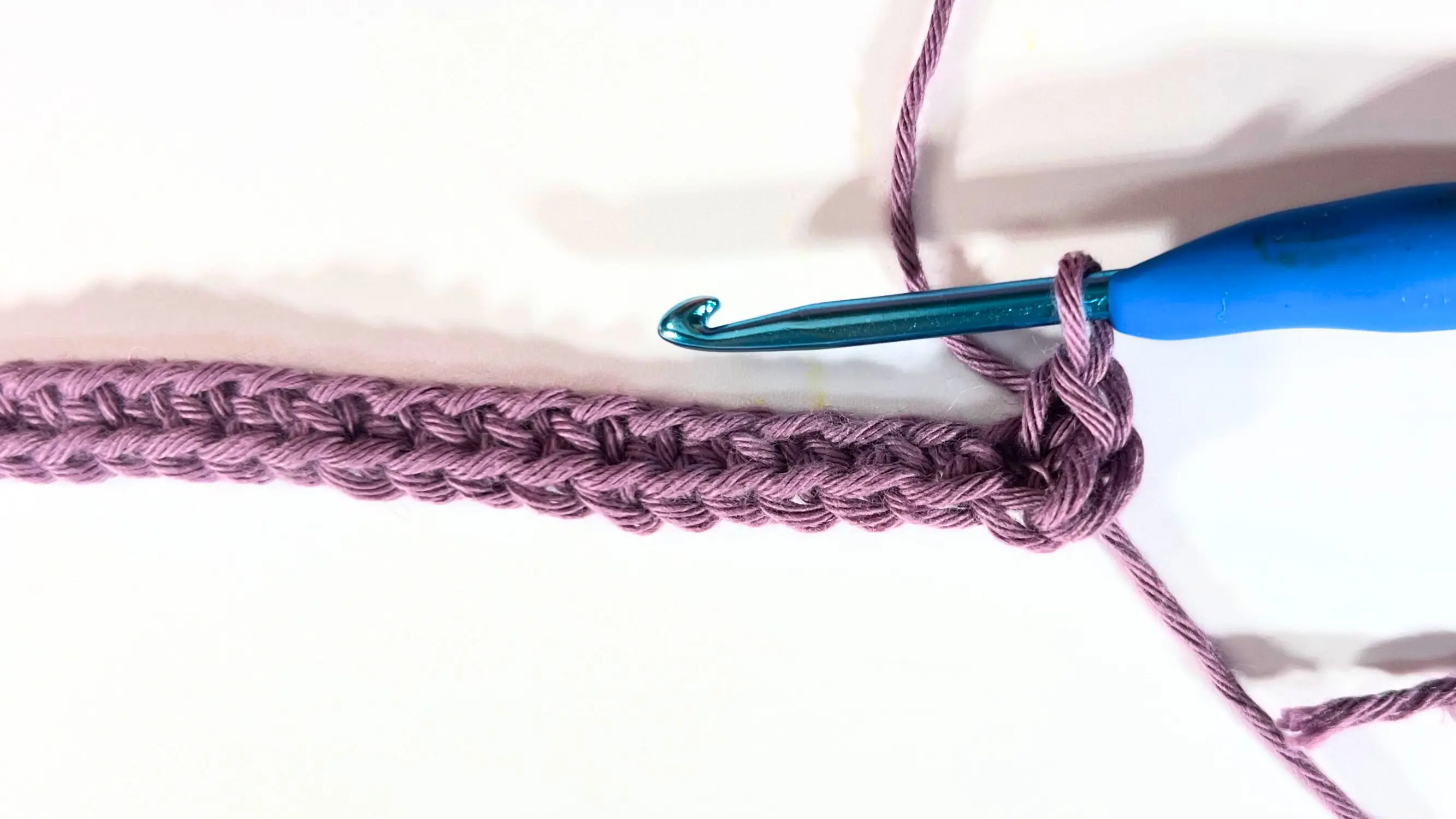 Close-up of crochet stitches forming the base row with purple yarn.