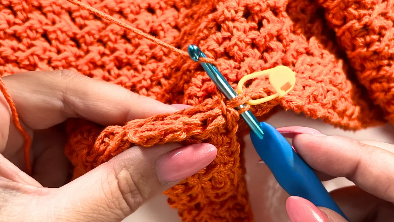 Inserting the crochet hook into the stitch marked with a yellow stitch marker to attach the strap on the opposite side of the summer top.