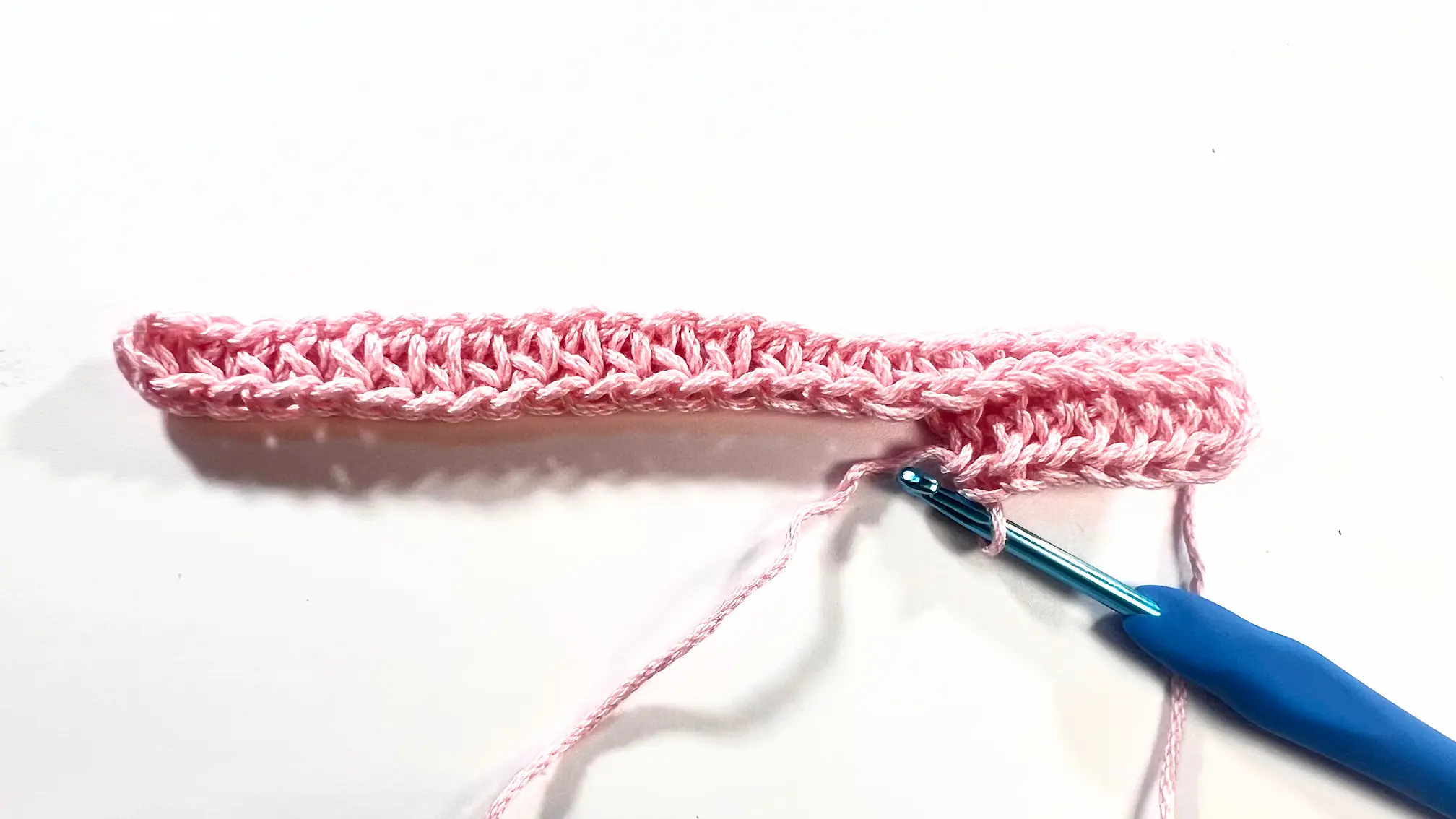 Progress of the second row in camel stitch using pink yarn, showing the ridged texture beginning to form on the reverse side.