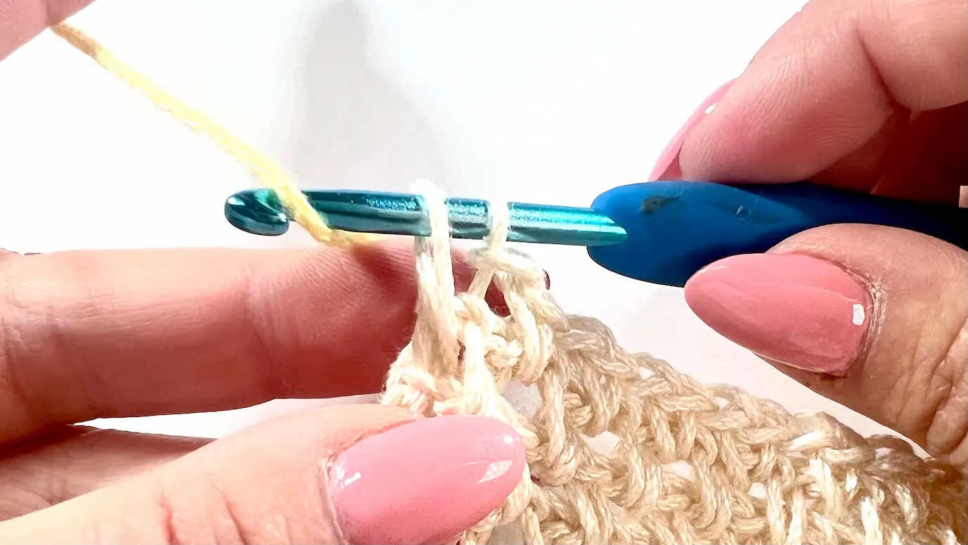 New yarn colour (yellow) is placed over the hook and pulled through both loops on the hook to complete the final SC in the old colour.