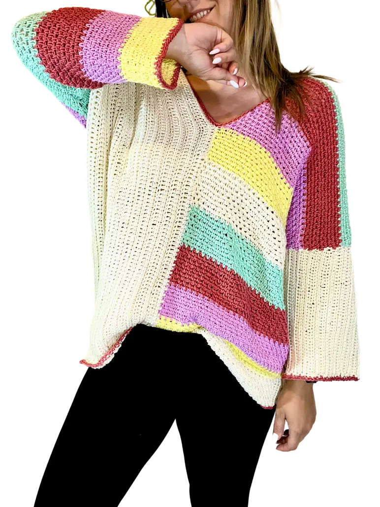 Model posing playfully in the Happy Stripes Sweater, a crochet design with bold colour blocks, soft drape, and roomy striped sleeves perfect for everyday comfort.