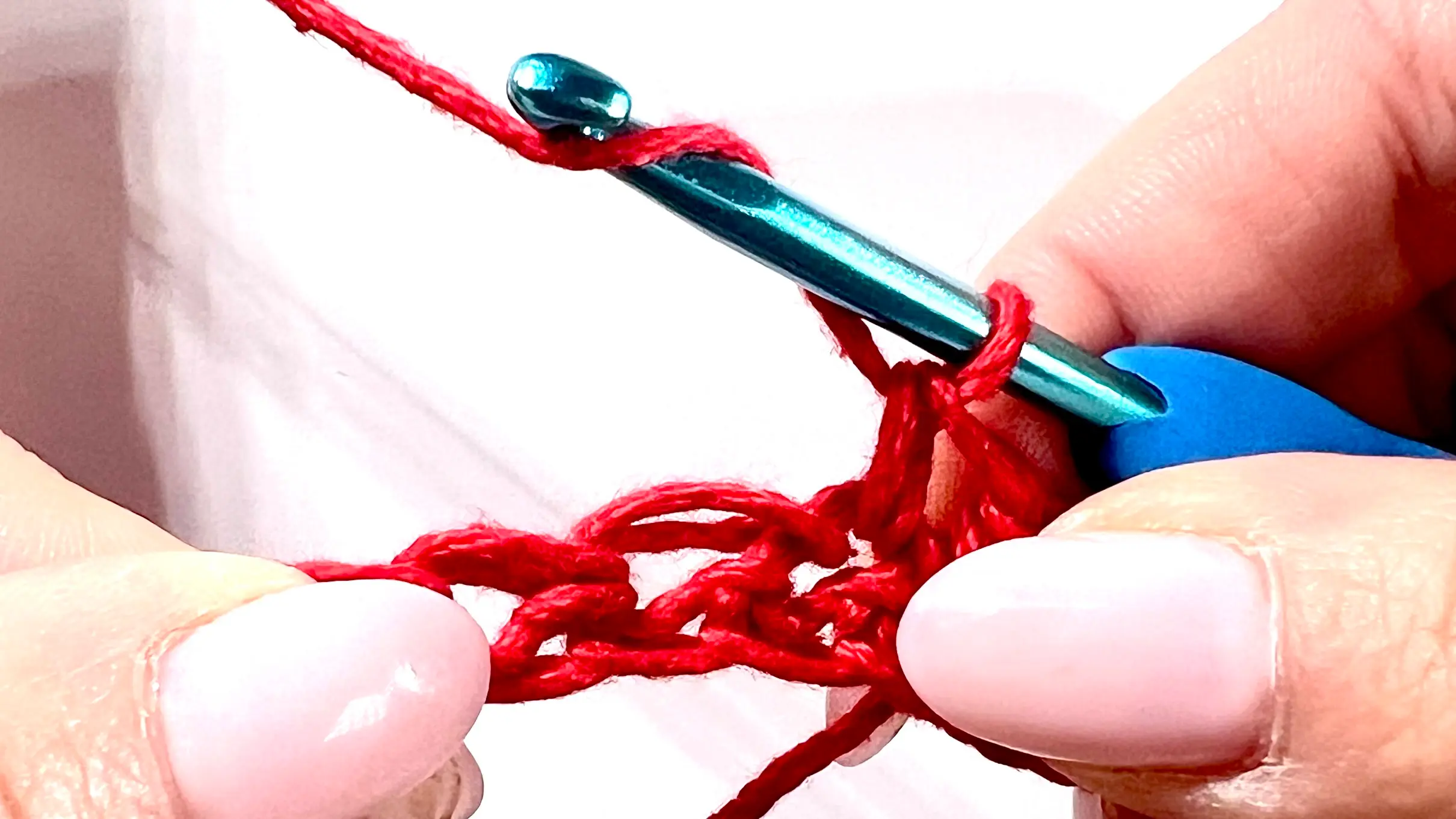Crocheter forming a bobble stitch in red yarn, with several incomplete double crochets on hook before closing the cluster.