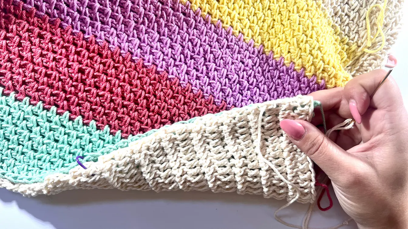 Crochet panels positioned wrong side out, with one hand holding the edges together and a yarn needle inserted for seaming, ensuring a neat finish on the right side.