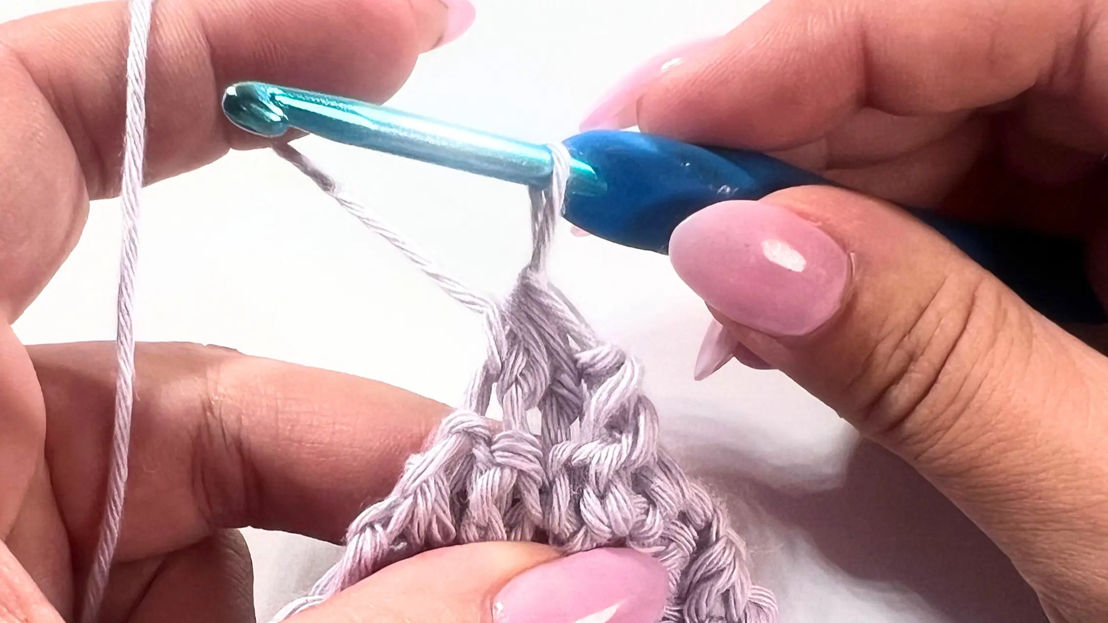 Crochet hook pulling yarn through all four loops to complete SC3tog decrease, neatly shaping the corner of the washcloth.