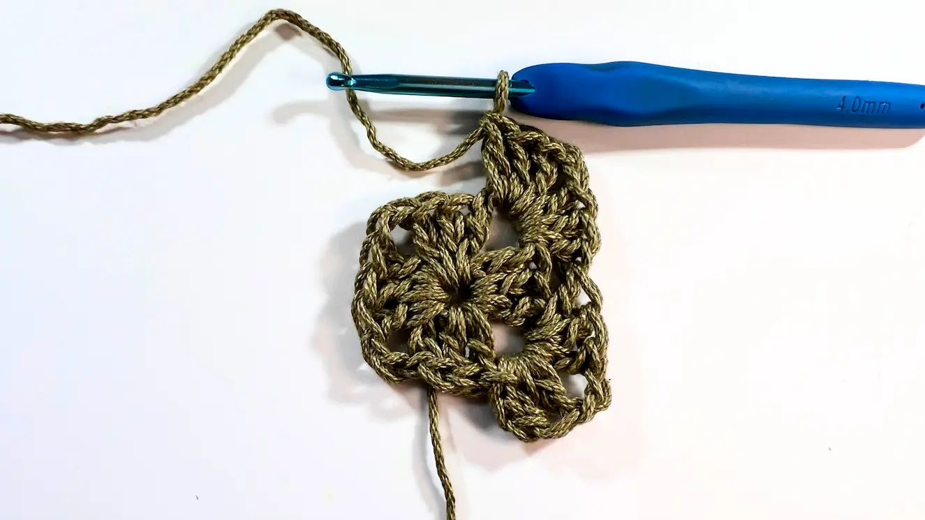 Crochet square with hook working into the next corner space to begin another corner cluster.