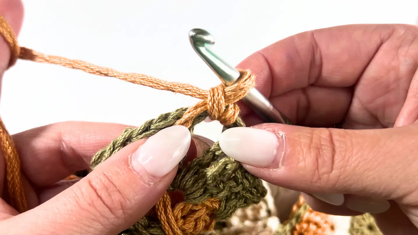 Orange yarn is attached to the hook, preparing for the first double crochet stitch into the chain space.