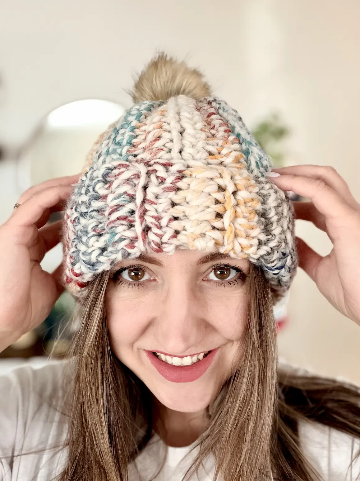Woman wearing chunky crochet beanie with folded brim and faux fur pompom, made from super bulky variegated yarn.