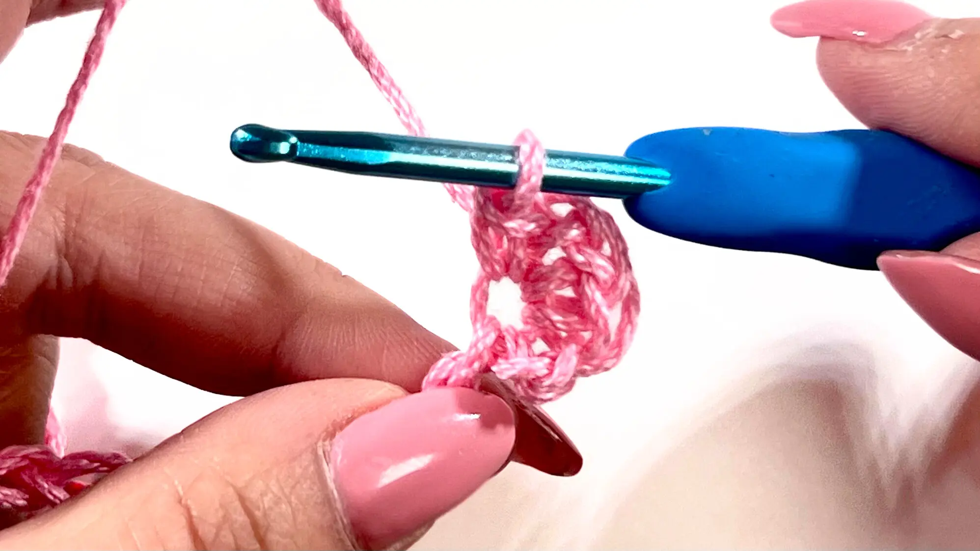 First Primrose Stitch cluster completed in pink yarn, shown on blue crochet hook between two hands.