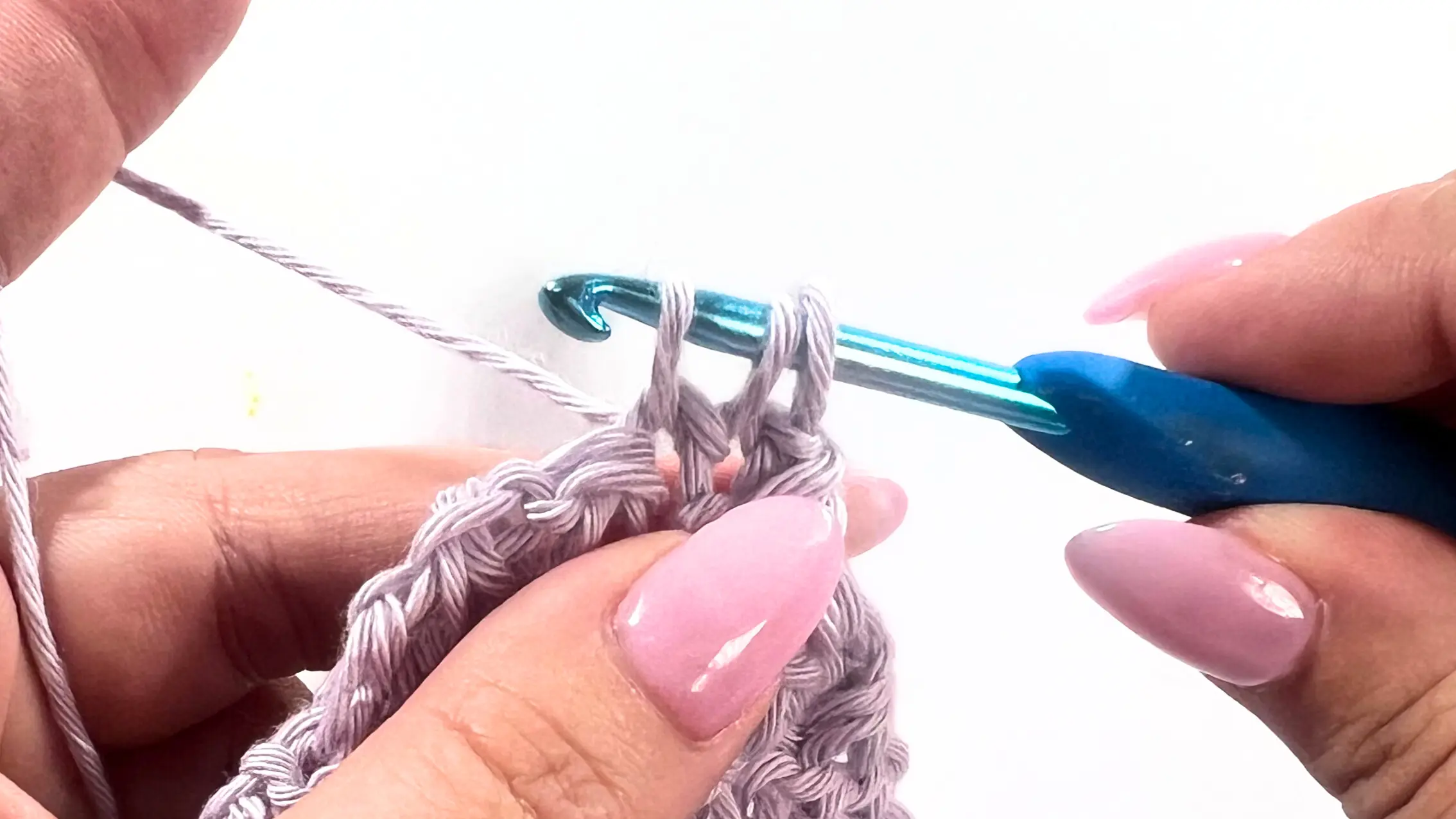 e-up of crochet hook pulling up loops in the second stitch, showing three loops on the hook for SC3tog decrease.