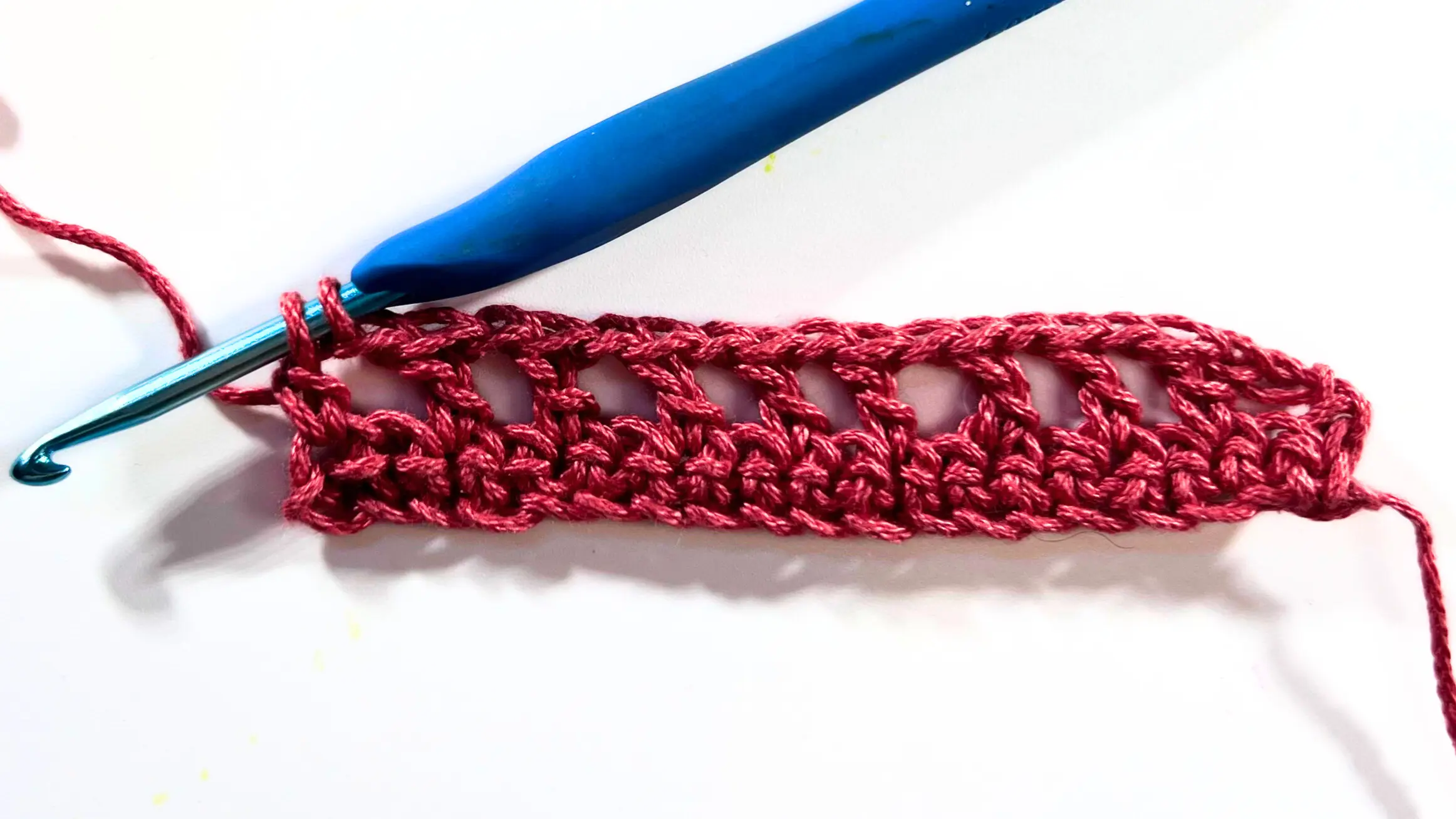 Crochet swatch in red yarn showing the final double crochet of the row worked only halfway, with two loops left on the hook.