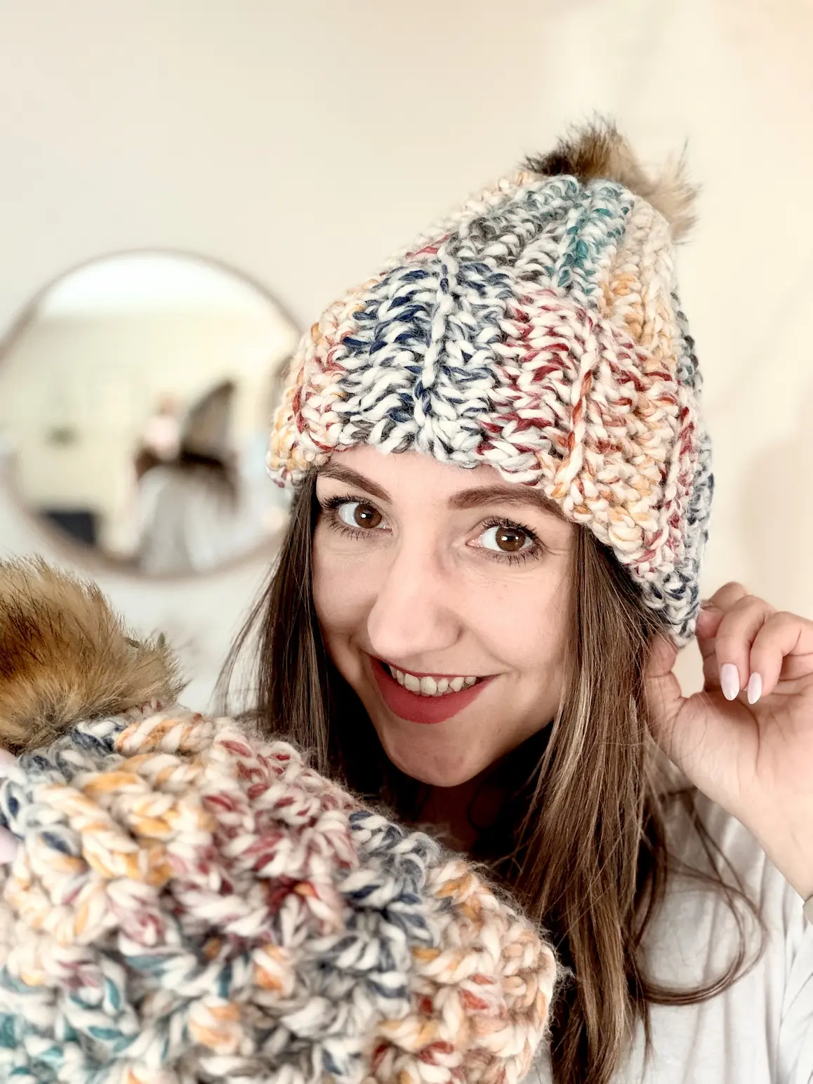 Woman modeling textured chunky crochet hat in super bulky yarn with folded brim and faux fur pompom.