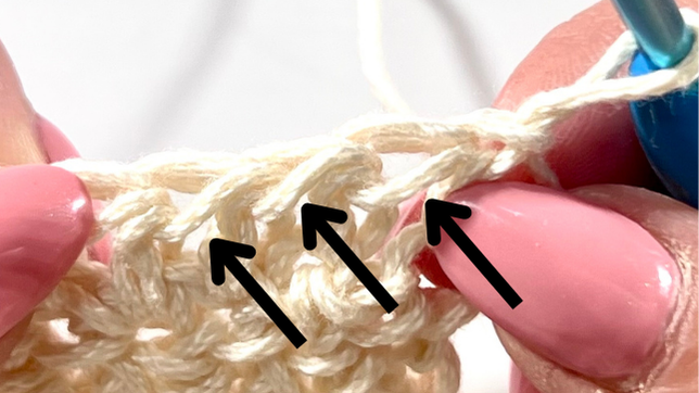 Close-up showing several stitches with arrows pointing to the very front loops, demonstrating where to insert the hook in each stitch for textured Half Double Crochet.