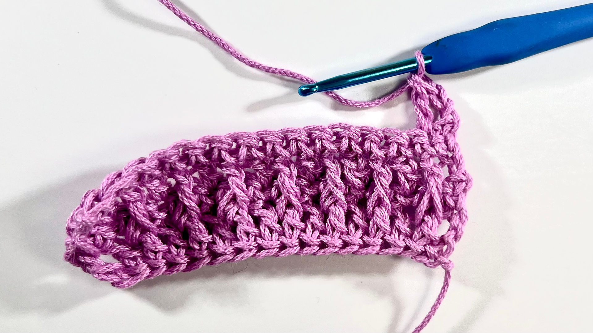 Crochet Alpine Stitch with pink yarn and blue crochet hook on a white background - Step 9