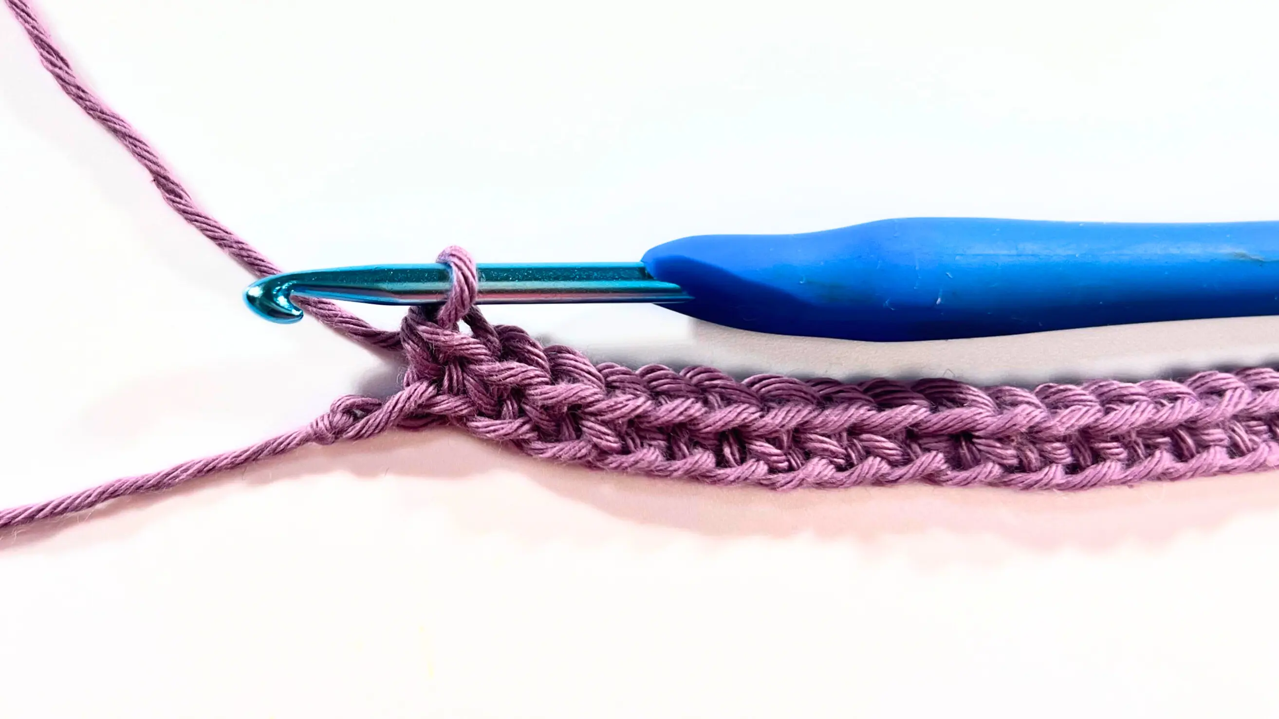 Crocheting first row of single crochet stitches with purple yarn and blue hook.