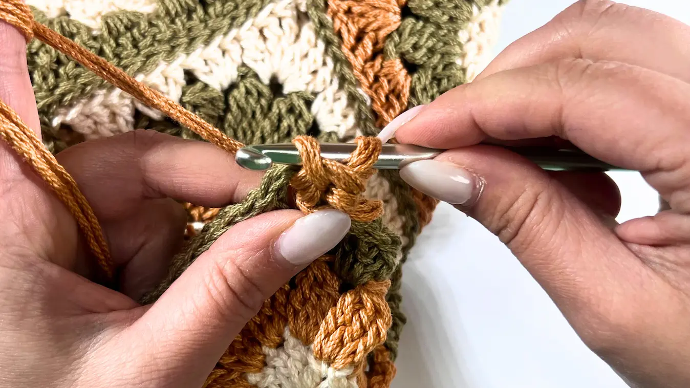 A crochet hook is inserted through the stitch with orange yarn as the strap grows longer.