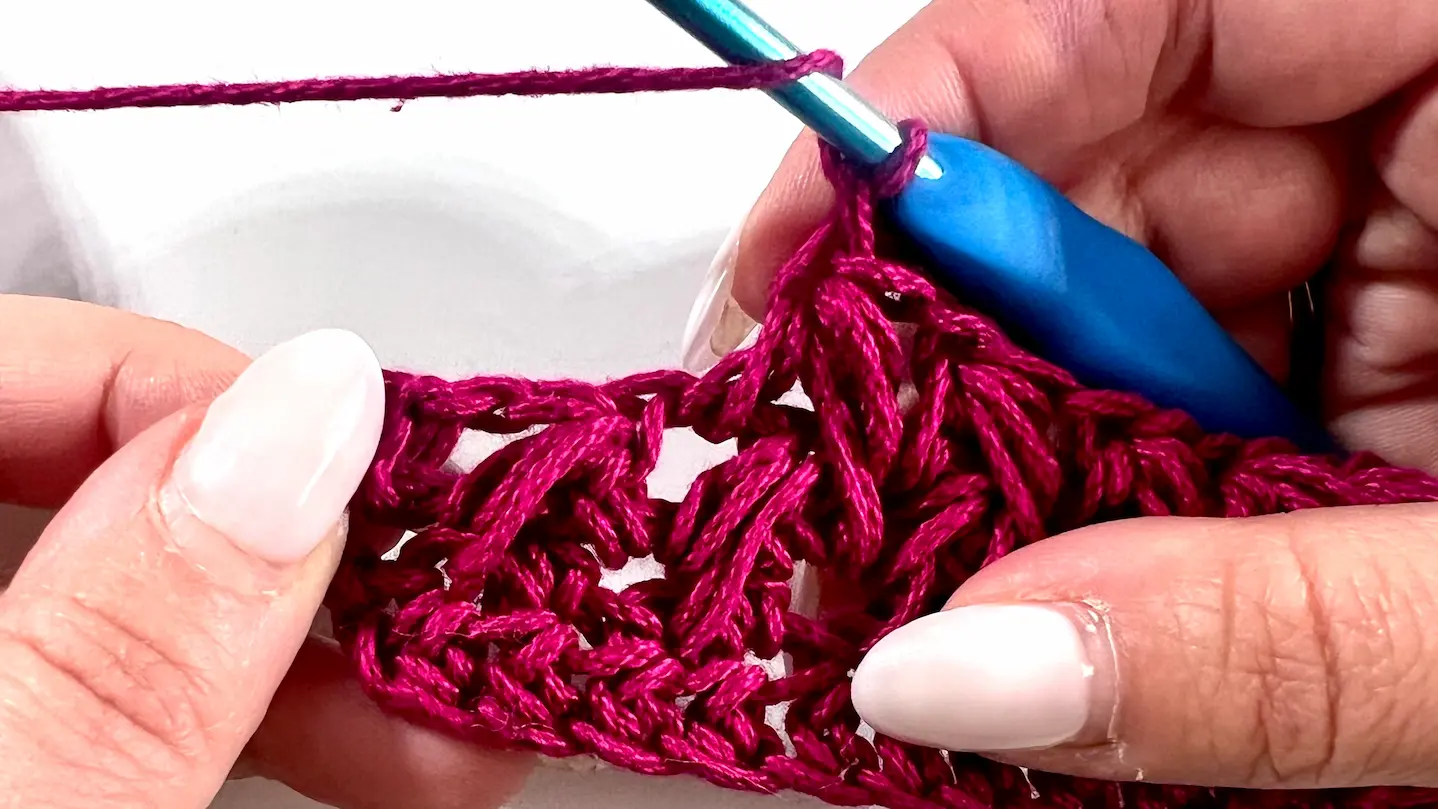 Close-up showing how to crochet the feather stitch step-by-step using fuchsia yarn and a blue crochet hook — part of a textured stitch tutorial.