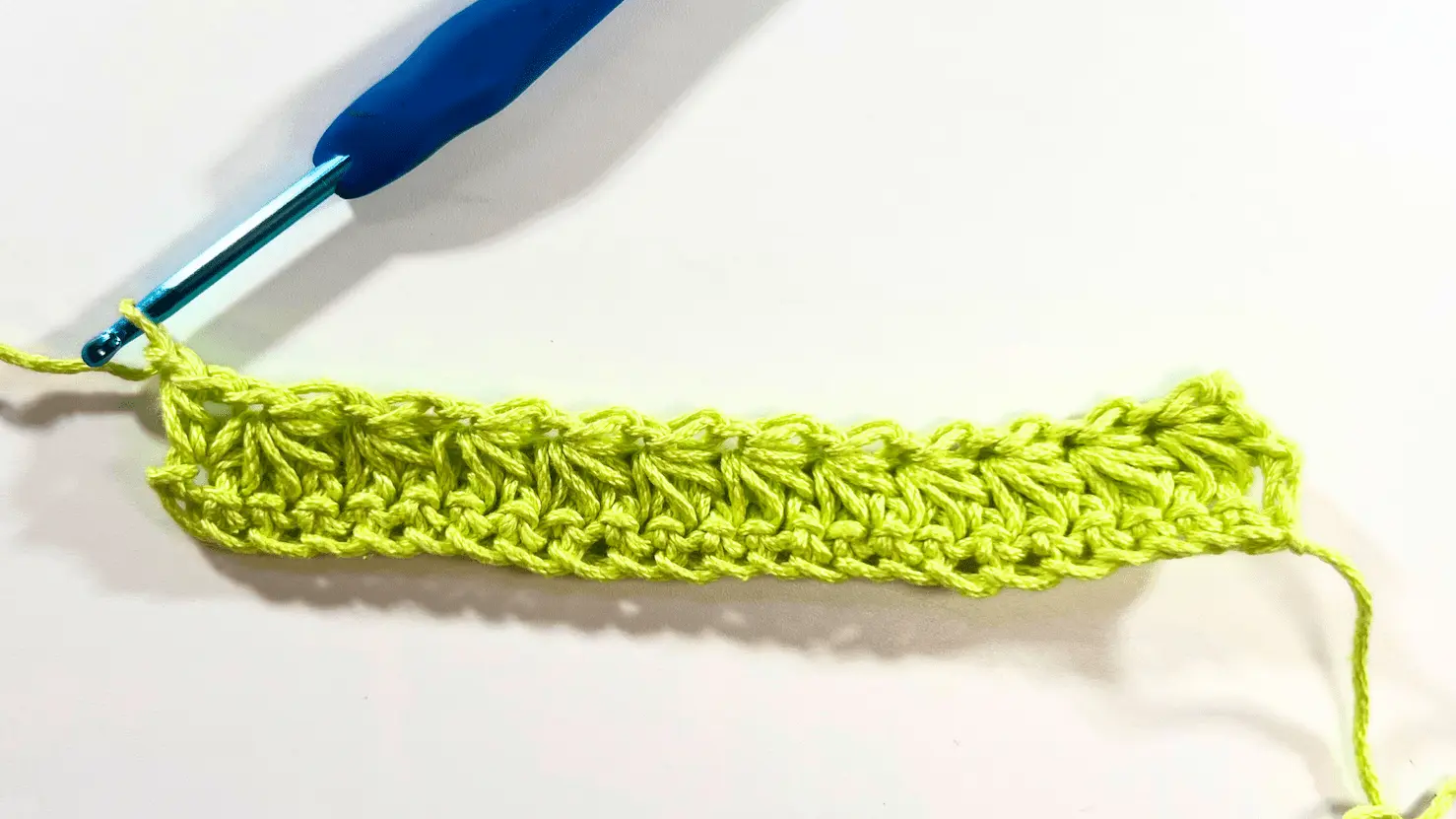 First row of Star Stitches completed in bright green yarn with a blue crochet hook; foundation row and top edge clearly visible.