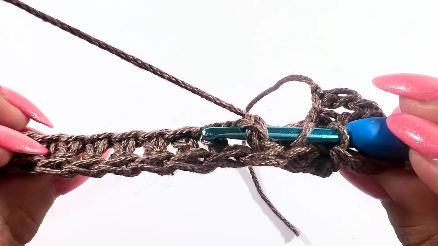 Close-up of a crochet hook placed behind the fabric and around the post, showing how to work a BPDC from the back side of the stitch.